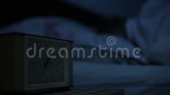 一个穿睡衣的女孩躺在床上看着闹钟睡不着从小时到小时的可变焦点视频的预览图