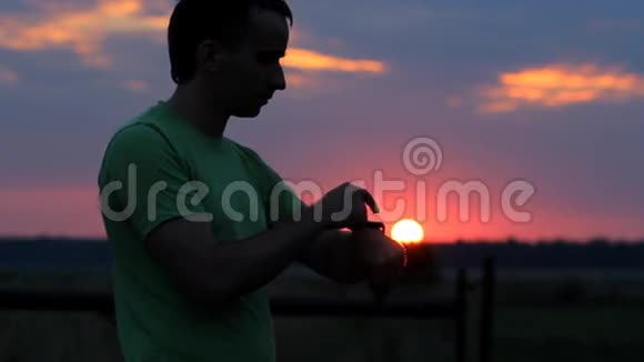 一个人在日落时看并触摸智能手表美丽的红天和树林后面的太阳视频的预览图
