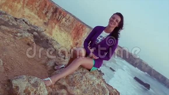 穿着紫色夹克短裤坐在岩石上的布鲁内特少女视频的预览图