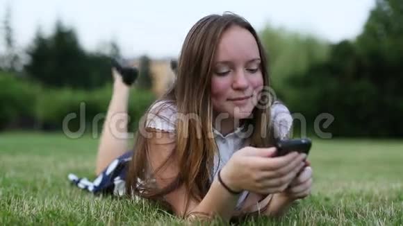 情绪化的少女躺在绿草上使用智能手机视频的预览图