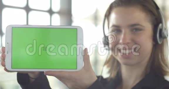 带耳机的女商人带绿色屏幕的独立平板电脑视频的预览图