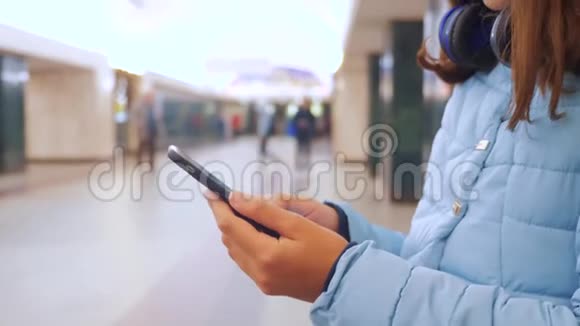 十几岁的女孩带着智能手机和耳机等待地铁很多人挤在地下十字路口的生活方式地铁视频的预览图