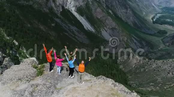 攀登高峰快乐的人拥抱举起双手在尖岩石崖蓝天背景空中缓慢视频的预览图