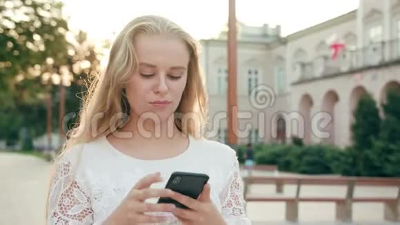 年轻的金发女郎在城里散步和使用电话视频的预览图