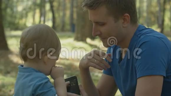 父亲在公园帮助哭泣的儿子使用手机视频的预览图