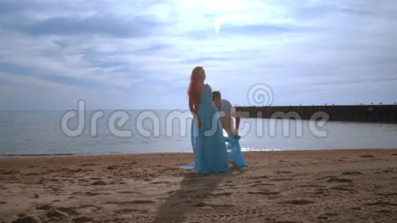 带着蓝色布料在海滩上飞翔的孕妇怀孕概念视频的预览图