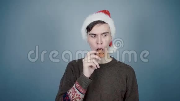 戴着圣诞帽的年轻人吃着灰色的饼干视频的预览图