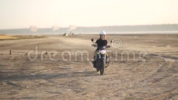 美丽的年轻女子骑着一辆古老的咖啡馆赛车摩托车在沙漠日落或日出女司机慢动作视频的预览图