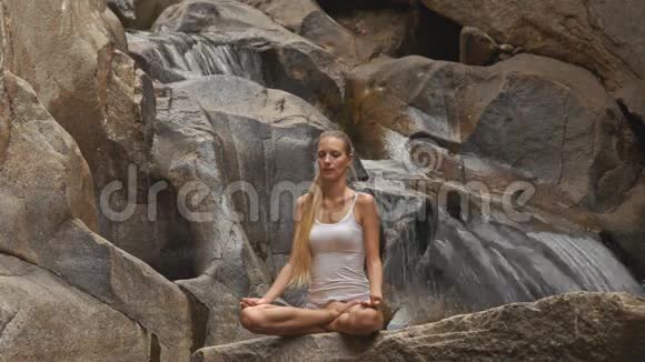 金发女郎坐在瀑布石上的瑜伽软管莲花中视频的预览图