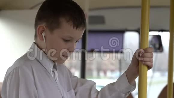 一个小男孩乘公共汽车穿过城市的特写镜头他用智能手机听音乐视频的预览图