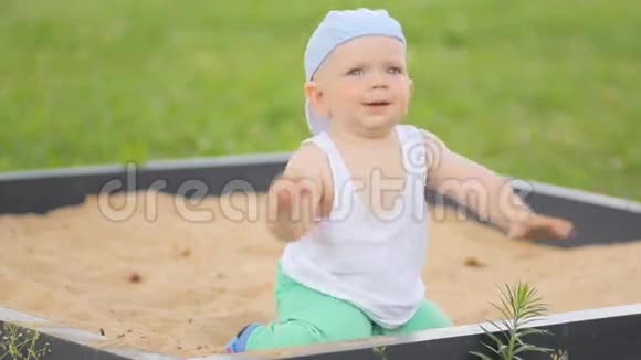 可爱的小男孩在沙箱里玩沙子夏日公园和背景中的绿草视频的预览图