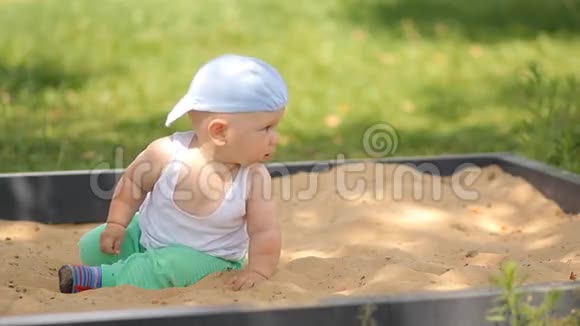 可爱的小男孩在沙箱里玩沙子夏日公园和背景中的绿草视频的预览图