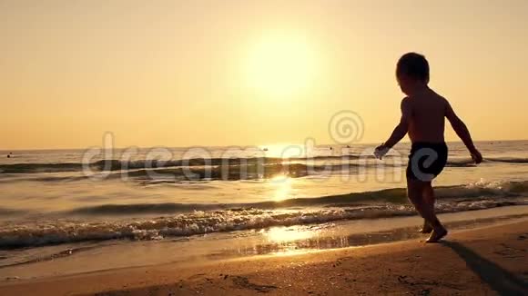 日落时海滩上的男孩剪影流入大海视频的预览图