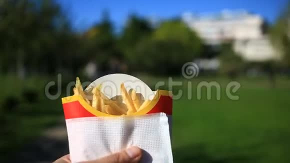 一个人在街上吃快餐他拿着一份薯条吃了它在一个模糊城市的背景下视频的预览图