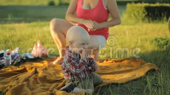 妈妈在公园里和小儿子玩他们坐在草地上的毯子上微笑着视频的预览图