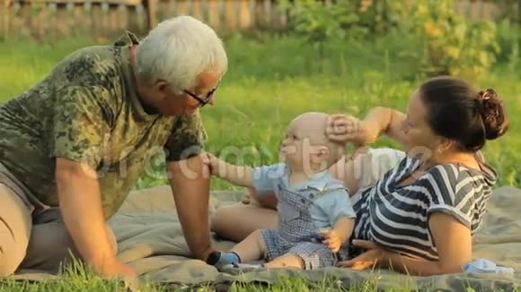 快乐的一家人在一个夏天的公园里和一个蹒跚学步的小男孩玩那里有美丽的草地妈妈宝贝爷爷视频的预览图
