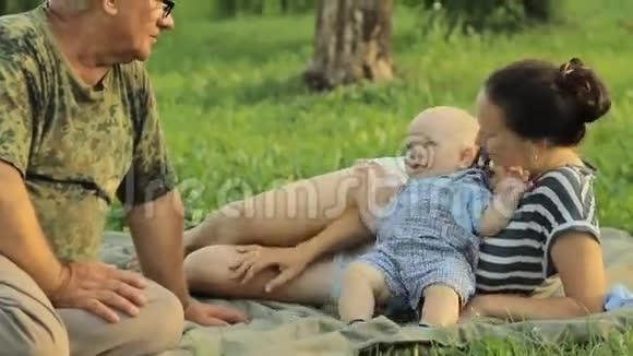 快乐的一家人在一个夏天的公园里和一个蹒跚学步的小男孩玩那里有美丽的草地妈妈宝贝爷爷视频的预览图