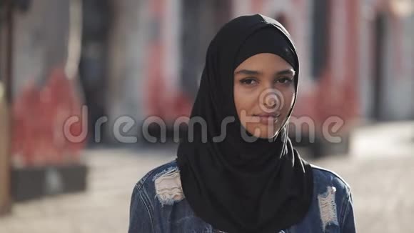 一幅美丽的穆斯林年轻女子戴着头巾微笑着站在老城区的镜头中的画像视频的预览图