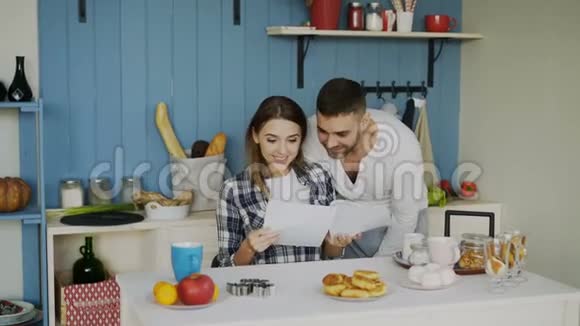 一对漂亮的幸福夫妇在家吃早餐时在厨房里收到一封正在展开的好消息视频的预览图