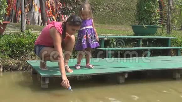 女人和女儿在池塘里喂鱼后备步行鹅很多鱼视频的预览图