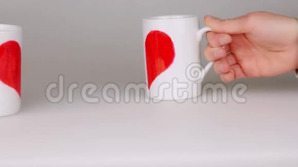 手拿着两个咖啡杯涂上一半的红色心形放在附近使一颗心视频的预览图