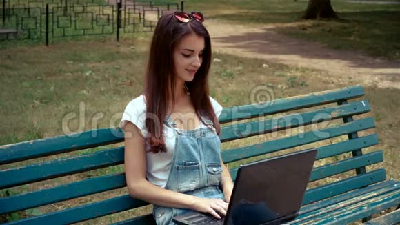 可爱的黑发女人坐在长凳上看着笔记本电脑视频的预览图