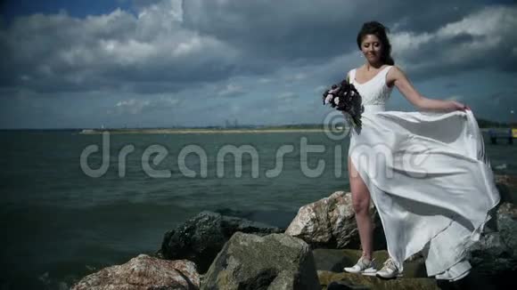溅起的水包裹着一个迷人的年轻女人新娘穿着白色连衣裙站在大海上手里拿着一束鲜花视频的预览图