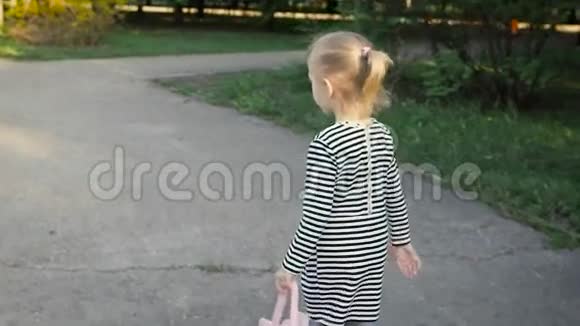快乐的童年可爱的金发女郎穿过公园她穿着一件条纹连衣裙视频的预览图