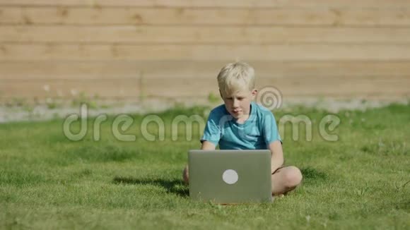 在草地上用笔记本电脑的男孩视频的预览图