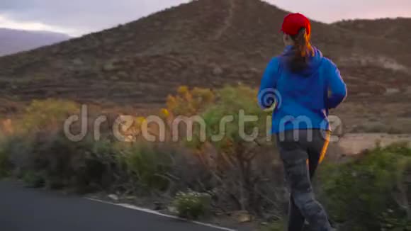 日落时分女人沿着荒芜的沥青路奔跑后景背景上的山脉视频的预览图
