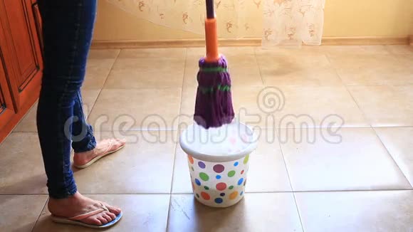 一个女人用拖把洗厨房里的地板在五颜六色的桶里蘸一块抹布视频的预览图