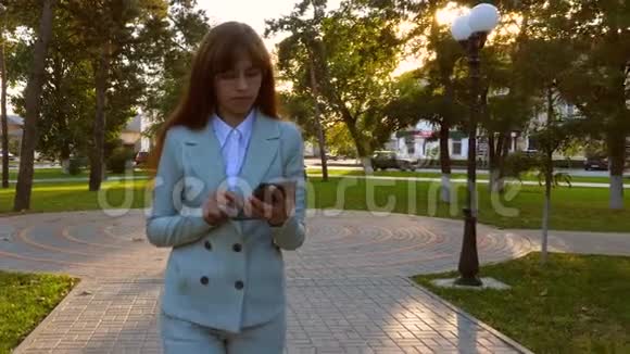 美丽的女商人走在公园的小巷里手里拿着平板电脑穿着轻便商务服的女孩去上班视频的预览图