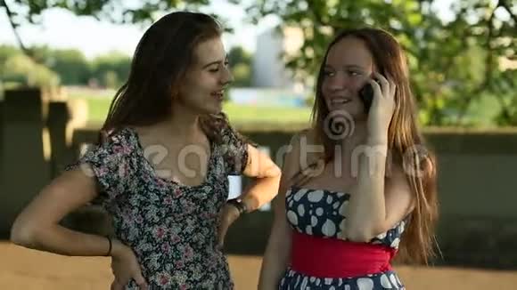 两个女孩站在公园里用手机说话视频的预览图