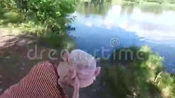 女孩在池塘的水里扔石头这个池塘位于老的杂草丛生的公园里视频的预览图