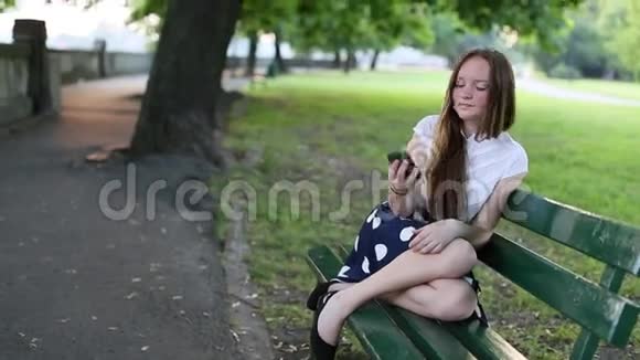 公园里坐在长凳上用智能手机自拍的少女行走视频的预览图