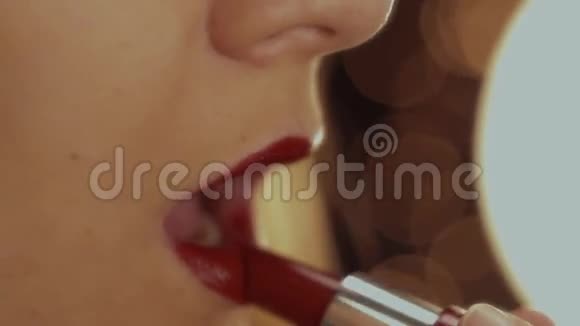 女孩把她的嘴唇涂成红色的口红在背景中从灯光中发光视频的预览图