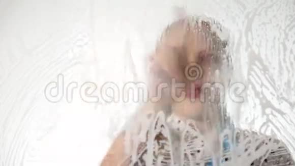 特写微笑的小家庭主妇用喷雾布和洗涤剂洗窗户泡沫中的大玻璃家务活视频的预览图