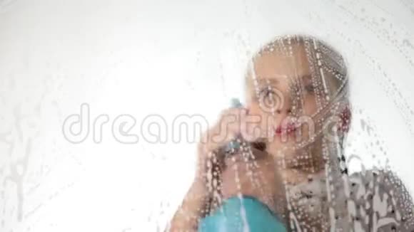 特写微笑的小家庭主妇用喷雾布和洗涤剂洗窗户泡沫中的大玻璃家务活视频的预览图