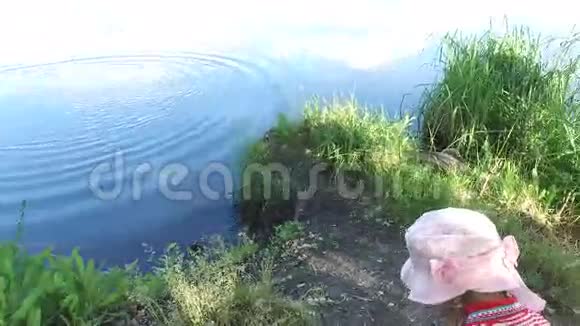 女孩在池塘的水里扔石头这个池塘位于老的杂草丛生的公园里视频的预览图