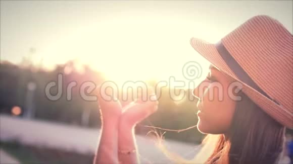 美丽的女人在日落时用手做心形女孩用橙色的太阳耀斑举起爱的象征姿态视频的预览图