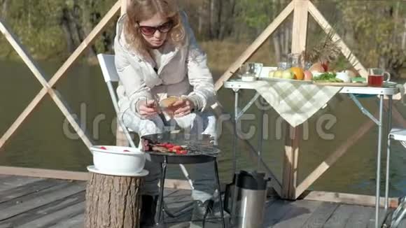 年轻女子穿着暖和的衣服在烤架上准备蔬菜和肉准备一个汉堡一只狗在附近玩耍一只视频的预览图