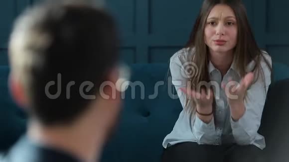 年轻女子在豪华的蓝色沙发上坐在舒适的沙发上看男心理学家视频的预览图