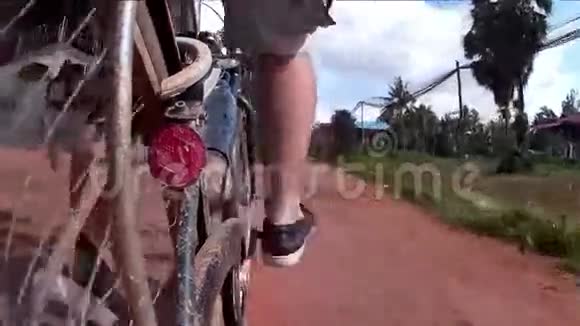 亚洲的一个骑自行车的人经过一个小村庄在一条农村土路上看到棕榈树后面安装的动作摄像头显示道路和小径视频的预览图