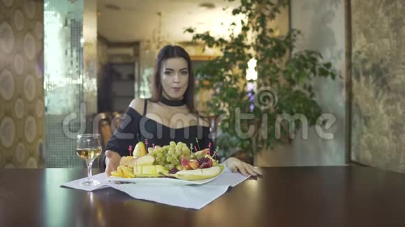 一位身着黑色礼服乳沟般的年轻女子独自在高档餐厅的餐桌上吃水果葡萄视频的预览图