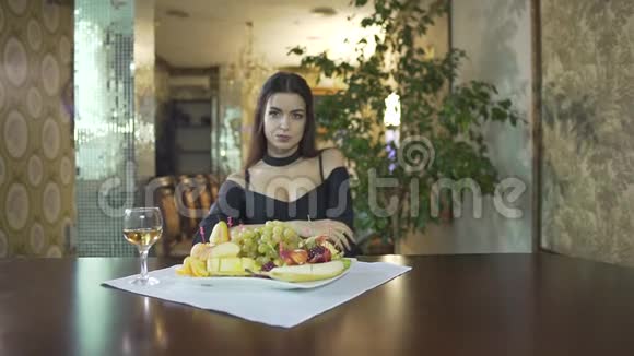 一个年轻的年轻的黑发女人穿着黑色的裙子乳沟独自吃水果葡萄在高档餐厅的餐桌上视频的预览图