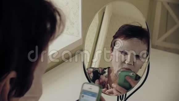 一位老妇人照镜子用化妆纸巾敷脸她用电话面部护理塑料视频的预览图
