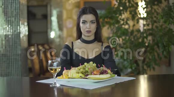 年轻迷人的黑发女人穿着黑色连衣裙乳沟独自吃水果葡萄一个人在高档餐厅吃饭视频的预览图