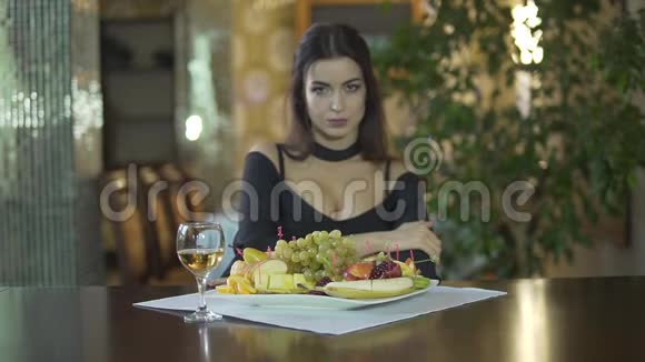 年轻迷人的黑发女人穿着黑色衣服乳沟独自在高档餐厅的餐桌上吃水果葡萄视频的预览图