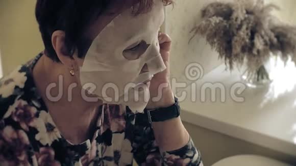 一位老妇人照镜子用化妆纸巾敷脸她用电话面部护理塑料视频的预览图