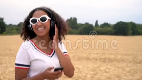 戴着白色太阳镜的年轻女子走在田野里用无线耳机听音乐视频的预览图